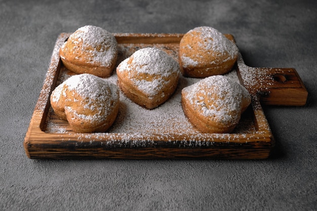 Hausgemachte Kuchen, Muffins mit Puderzucker, auf einem Holzbrett, auf einem grauen Tisch