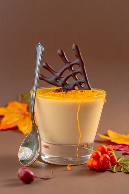 Hausgemachte Kürbis Panna Cotta mit Orangengelee serviert mit Schale und Schokoladendekor auf einem braunen Hintergrund mit Kopienraum. Idee einer Halloween-Party.