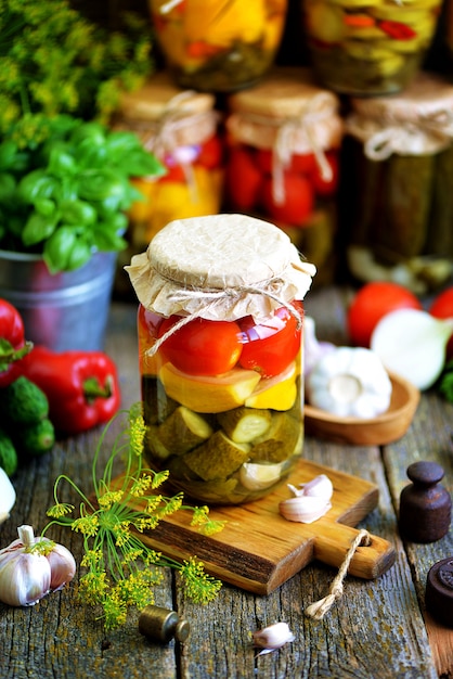 Hausgemachte marinierte sortiert mit Tomate, Gurke und Kürbis, Dill, Karotte, Knoblauch und Zwiebel in einem Glas auf einem alten hölzernen Hintergrund. Rustikaler Stil.