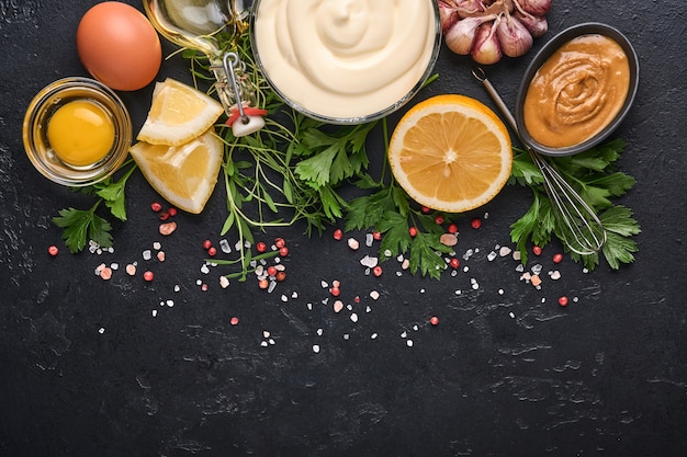 Hausgemachte Mayonnaise-Sauce und Zutaten Zitrone, Eier, Olivenöl, Gewürze und Kräuter, schwarzer Hintergrundkopierraum. Essen kochen Hintergrund. Ansicht von oben.