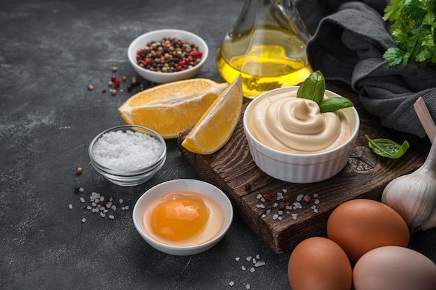 Hausgemachte Mayonnaise und Zutaten auf dunklem Hintergrund. Seitenansicht, Kopienraum.