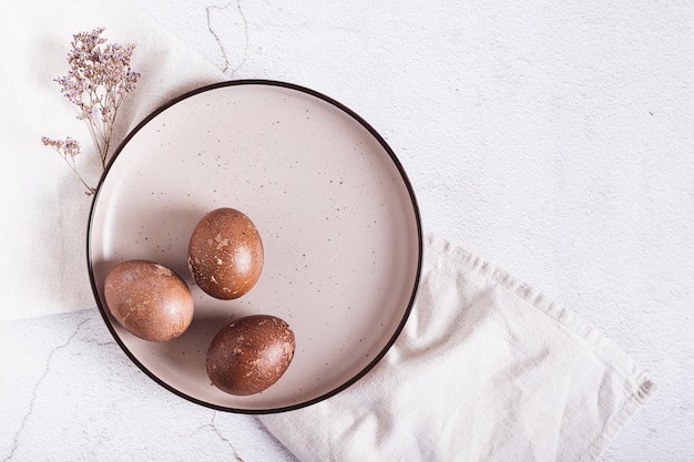 Hausgemachte natürliche bemalte Eier für Ostern auf einem Tellertuch und getrocknete Blumen oben