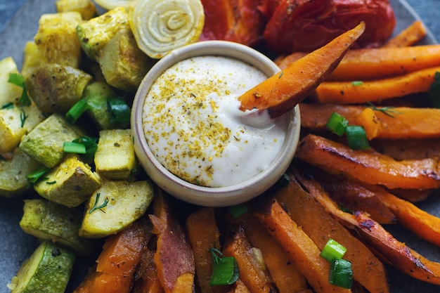 Hausgemachte, ofengebackene Süßkartoffeln mit Tomaten, Zwiebeln, Paprika und Soße auf dunklem Steintisch, gesundes Ernährungskonzept, weicher Fokus