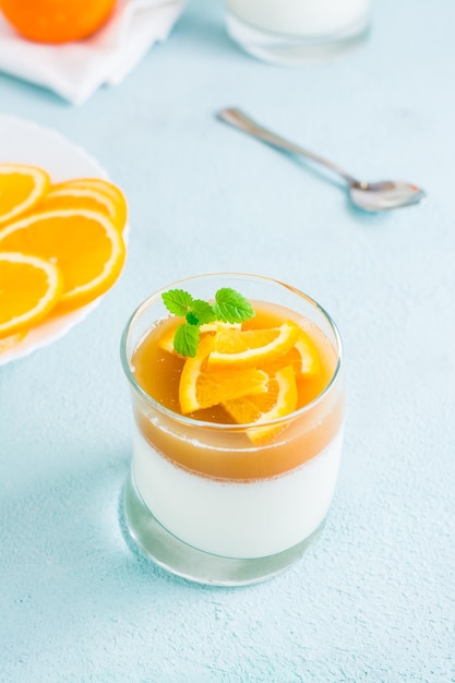 Hausgemachte Panna Cotta mit Orangen- und Minzblatt in einem Glas auf einem Leuchttisch Süßes italienisches Dessert Vertikale Ansicht Nahaufnahme