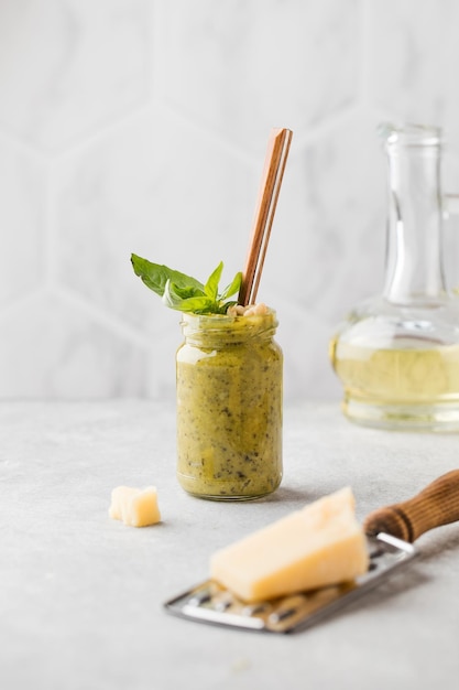 Hausgemachte Pesto-Sauce in einem Glas mit einem Löffel mit Basilikumblättern Parmesan und Olivenöl im Hintergrund italienische Küche