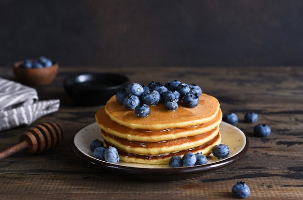 Hausgemachte Pfannkuchen auf Holzuntergrund mit Honig und Blaubeeren.