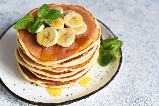 Hausgemachte Pfannkuchen mit Banane, Honig und Minze auf dem Küchentisch.