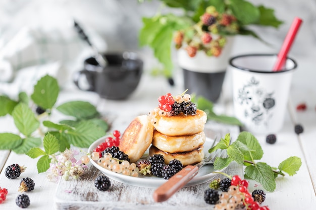 Hausgemachte Pfannkuchen mit Beeren und Wecker auf weißem Holz