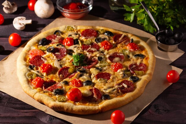 Hausgemachte Pizza mit Salami, Pilzen und Kirschtomaten auf dunklem Hintergrund. Seitenansicht.
