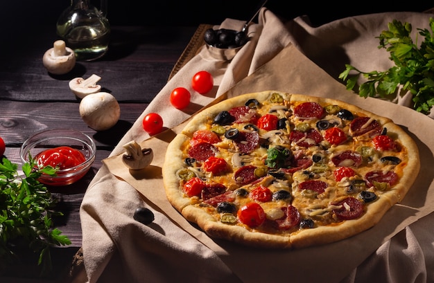 Hausgemachte Pizza mit Salami, Pilzen und Kirschtomaten auf dunklem Hintergrund. Seitenansicht.
