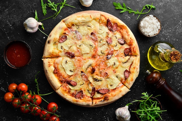 Hausgemachte Pizza mit Würstchen, Pilzen und Käse auf schwarzem Steinhintergrund Freier Platz für Text