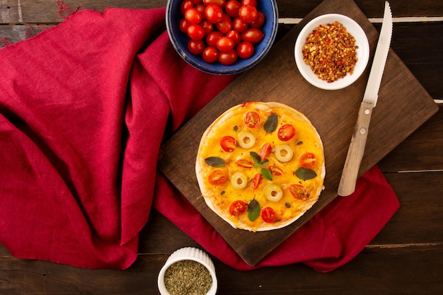 Hausgemachte Pizza-Pfanne mit Tomaten, Basilikum und Oliven in einem handgefertigten Holztisch mit Gewürzen und einem Messer