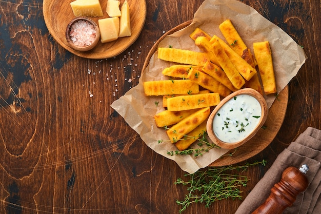 Hausgemachte polenta pommes frites mit meersalz, parmesan, thymian, rosmarin mit joghurtsauce. typisch italienische frittierte polenta. gebratene maisstäbchen. hölzerner hintergrund. ansicht von oben