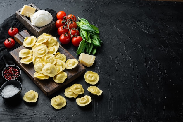 Hausgemachte Ravioli mit Mozzarella-Käse und Basilikum-Set, auf Holzschneidebrett, auf schwarzem Tisch,