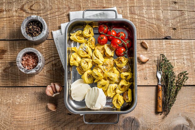 Hausgemachte rohe Ravioli mit Mozzarella-Käse und Tomate im Küchentablett. Hölzerner Hintergrund. Ansicht von oben.