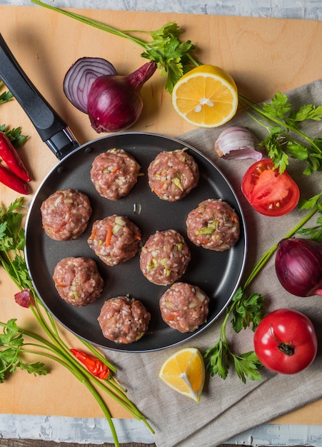 Hausgemachte rohe Rindfleisch Frikadellen auf einer Pfanne, vor dem Kochen, mit Gemüse.