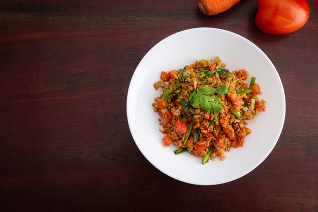 Hausgemachte Rühreier mit Karotten und Tomaten in weißer Platte auf Holztisch.