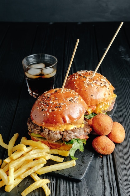 Hausgemachte saftige Burger auf Holzbrett, Käsebällchen. Streetfood, Fastfood. mit Pommes frites und einem Glas Cola. Ansicht von oben