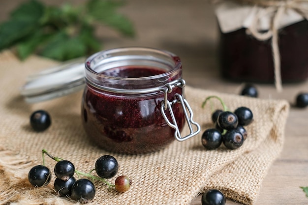 Hausgemachte schwarze Johannisbeermarmelade und frische Beeren auf Holzhintergrund Hausgemachtes Konservierungskonzept