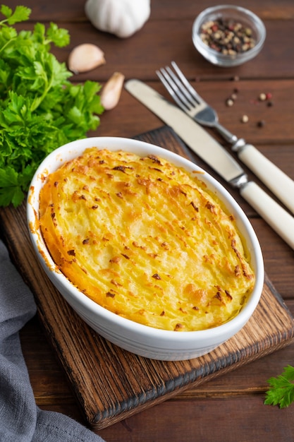 Hausgemachte Shepherd's Pie in der Auflaufform auf dunklem Holzhintergrund. Traditionelles britisches Gericht mit Hackfleisch und Kartoffelpüree.