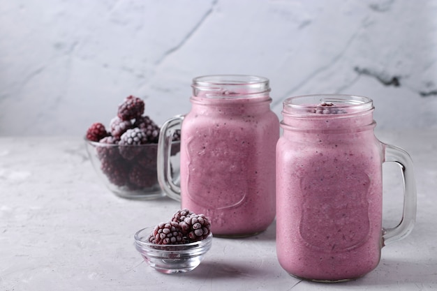 Hausgemachte Smoothies mit gefrorenen Brombeeren in Gläsern auf grauem Beton