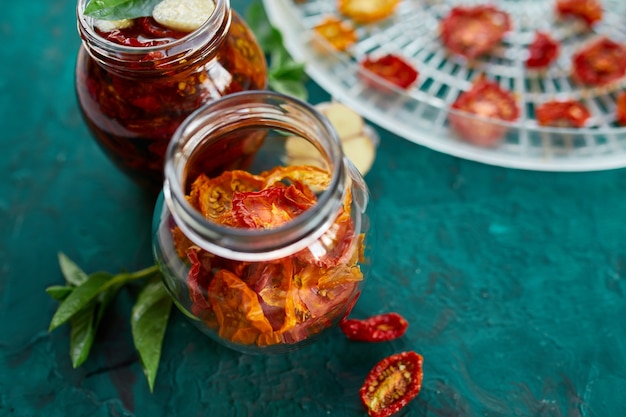 Hausgemachte sonnengetrocknete Tomaten mit Kräutern, Knoblauch in Olivenöl in einem Glas auf dunkelgrünem Hintergrund. Draufsicht. Druck für die Küche