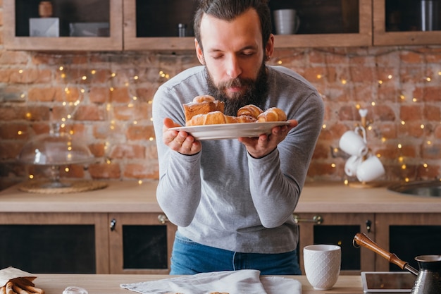 Hausgemachte süße Bäckerei. Junger bärtiger Mann mit geschlossenen Augen erfreut, wenn er frisches Gebäck riecht.