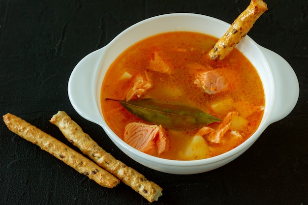 Hausgemachte Suppe mit Lachs mit Brotstäbchen auf konkretem Hintergrund.