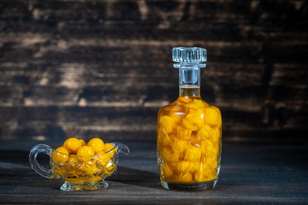 Hausgemachte Tinktur aus gelber Kirschpflaume in einer Kristallflasche auf Holzhintergrund, Ukraine, Nahaufnahme. Konzept für alkoholische Getränke mit Beeren