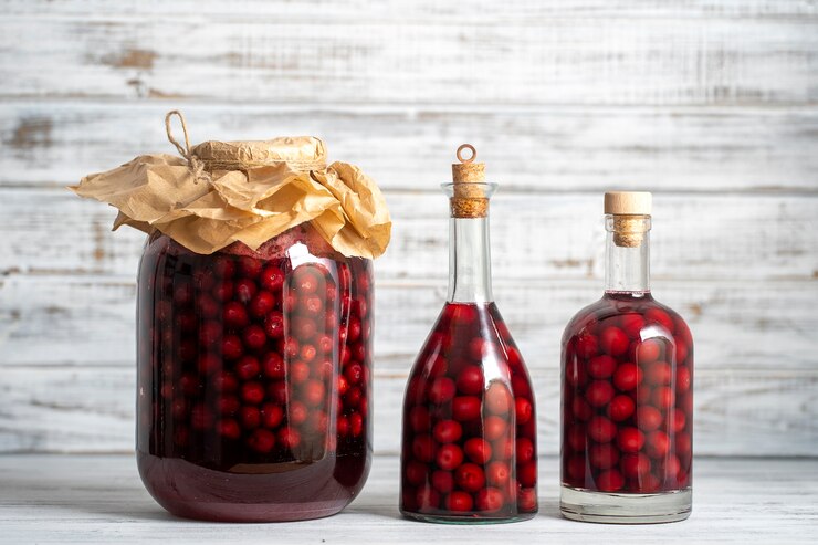 Hausgemachte Tinktur aus roten Kirschen. Beerenalkoholisches Getränkekonzept. Hausgemachter Rotwein aus reifen Kirschen in Glasflaschen und Gläsern