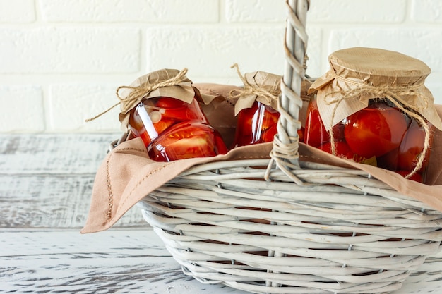 Hausgemachte Tomatenkonserven in Gläsern im weißen Weidenkorb auf Holzhintergrund.