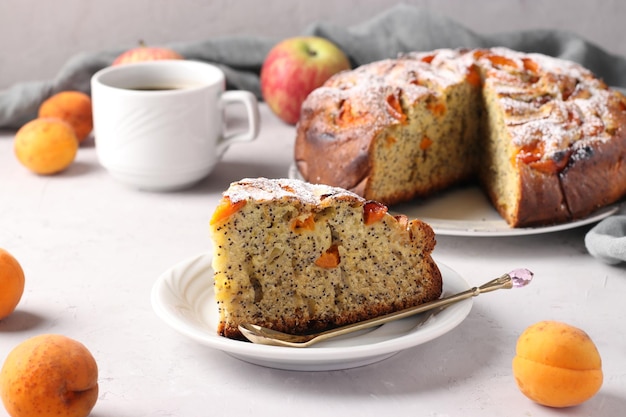 Foto hausgemachte torte mit mohn, aprikosen und äpfeln mit einer tasse kaffee auf grauem hintergrund