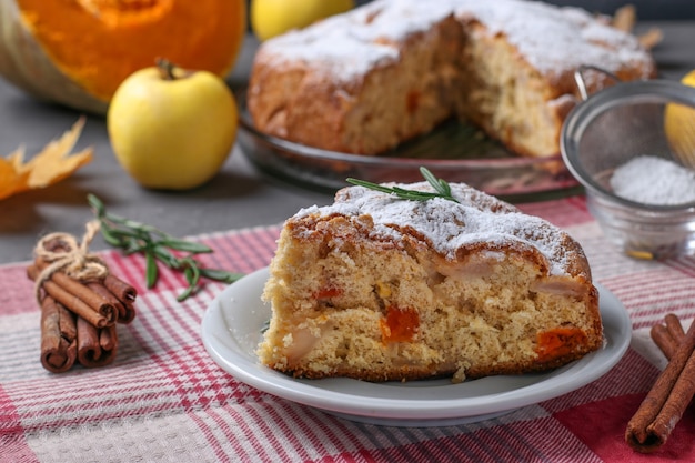 Hausgemachte Torte mit Äpfeln und Kürbis bestäubt mit Puderzucker auf weißem Teller.