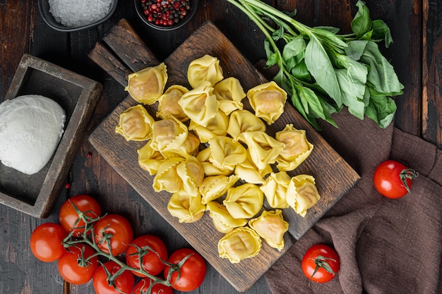 Hausgemachte Tortellini mit Käse-Basilikum-Set, auf Holzschneidebrett, auf altem dunklem Holztisch, Draufsicht flach gelegt