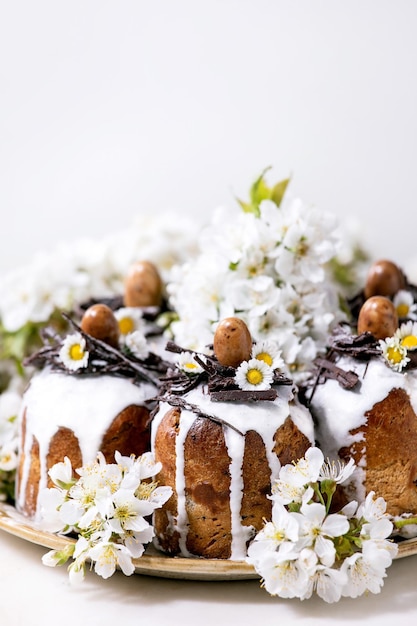 Hausgemachte Traditionla Osterkuchen mit Schokoladenestern und Eiern auf Keramikplatte und blühendem Kirschbaum auf weißem Hintergrund Traditioneller orthodoxer russischer Ukrainischer Osterkuchen Close up