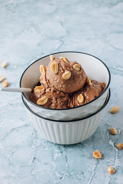 Hausgemachte vegane Erdnussbutter-Bananen- und Schokoladen-Eis in einer Schüssel mit Erdnüssen auf grauem Marmorgrund