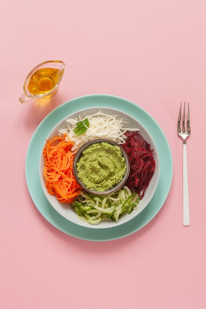 Hausgemachte vegetarische Poke Bowl frische rohe Karotten, Kohl, Gurken, Rüben und Pesto, Ernährung, gesundes Essen auf rosa Pastellhintergrund. Ansicht von oben, Nahaufnahme