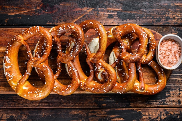 Hausgemachte weiche Brezeln mit Salz auf einem Holzbrett. Dunkler hölzerner Hintergrund. Ansicht von oben.