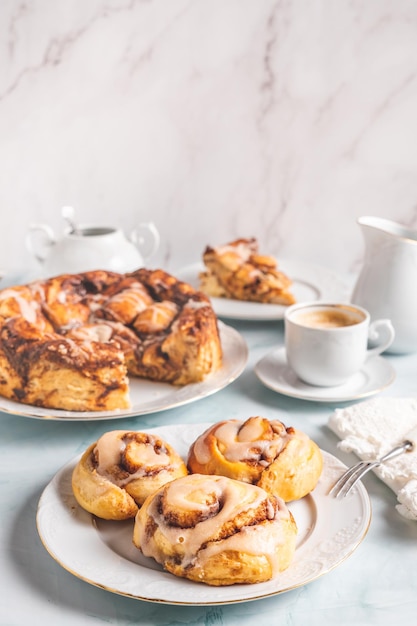 Hausgemachte Zimtbrötchen auf einem weißen Teller auf einem weißen Tisch mit Kaffee- und Gebäckbrötchen zum Frühstück