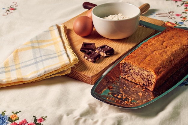 Hausgemachter Biskuitkuchen auf einer weißen Tischdecke mit einigen Zutaten, Eiern, Schokolade und Mehl