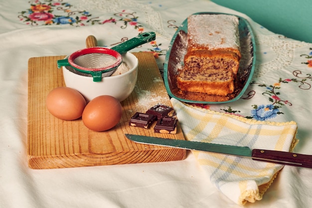 Hausgemachter Biskuitkuchen auf einer weißen Tischdecke mit einigen Zutaten, Eiern, Schokolade und Mehl