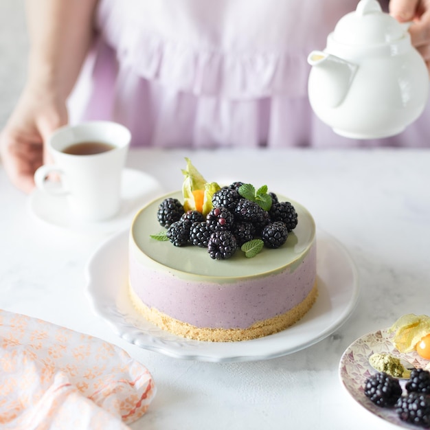 Hausgemachter Brombeer-Käsekuchen und Matcha-Tee auf dem festlich gedeckten Tisch Das Mädchen gießt Tee Square