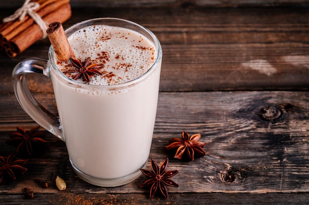 Hausgemachter Chai Tea Latte mit Anis und Zimtstange im Glasbecher auf rustikalem Holzhintergrund