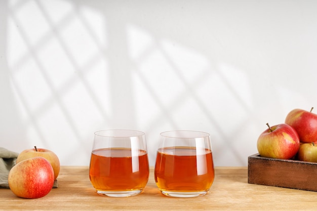 Hausgemachter frischer Apfelsaft in zwei Gläsern und frischen Äpfeln auf Holztisch Fensterschatten