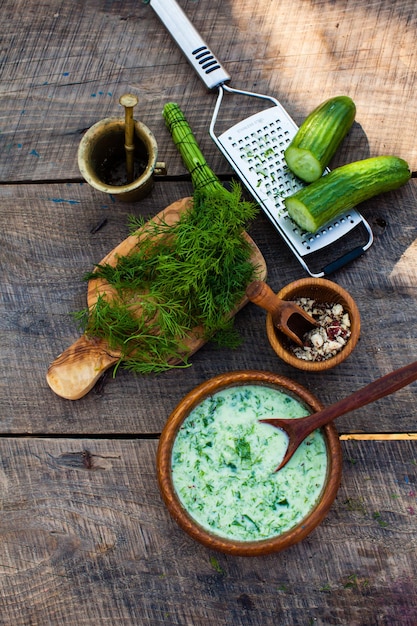 Hausgemachter gekühlter Tarator mit Zutaten auf rustikalem Holzhintergrund. Traditionelle bulgarische kalte Sommersuppe mit Gurken, Dill, Knoblauch, Joghurt und Walnüssen.