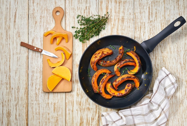 Hausgemachter gerösteter Butternusskürbis und Thymiankraut in gusseiserner Pfanne auf weißer Holztischplatte