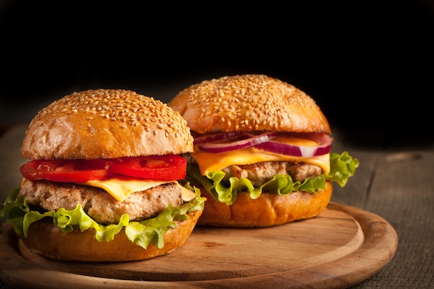 Hausgemachter hamburger mit rindfleisch, zwiebeln, tomaten, salat und käse. frischer burger nah oben auf rustikalem holztisch mit kartoffelpommes, bier und pommes. cheeseburger.