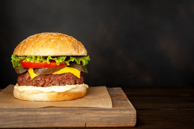 Hausgemachter Hamburger mit Salat, Tomate, Käse und Gurke auf einem Schneidebrett mit Kopierraum für Ihren Text