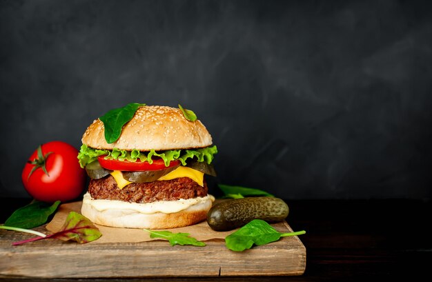 Hausgemachter Hamburger mit Salat, Tomate, Käse und Gurke auf einem Schneidebrett mit Kopierraum für Ihren Text