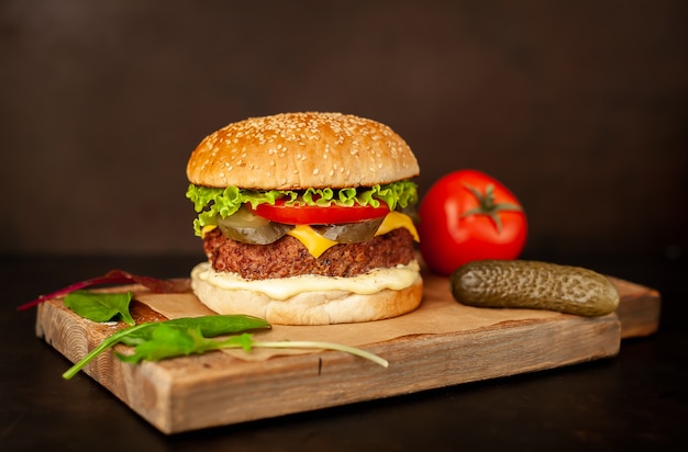 Hausgemachter Hamburger mit Salat, Tomate, Käse und Gurke auf einem Schneidebrett